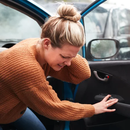 A young woman climbing out of her car after an accident, holding her neck in pain